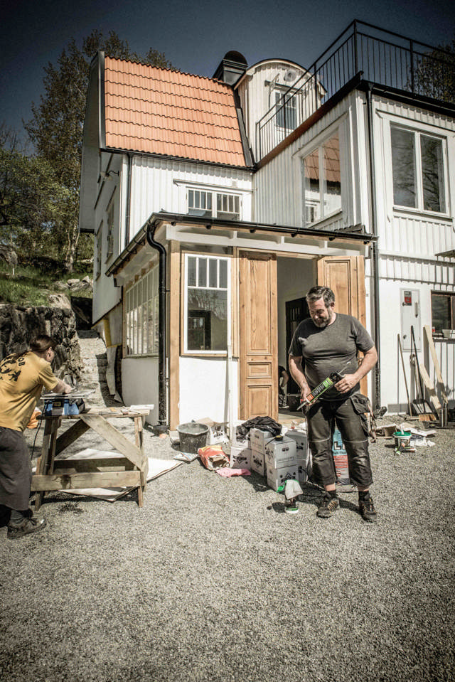 Ett vitt hus med en nybyggd veranda, framför huset syns byggprylar och en snickare.