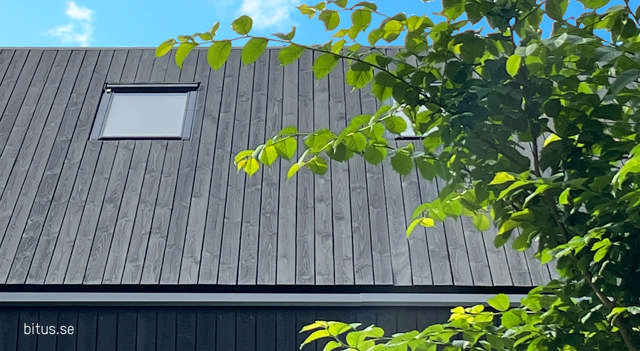 Närbild på ett hus klätt i svart träpanel där det zoomats in på ett takfönster.