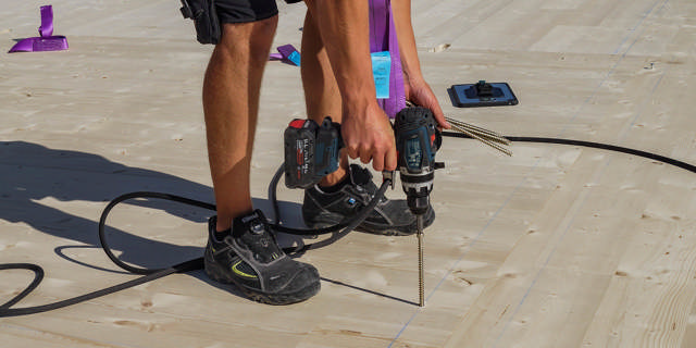 Montör med sele håller i konstruktionsskruv och skruvdragare.