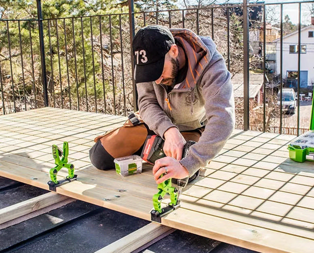 Snickare sitter på knä på ett trädäck och skruvar fast trallbrädor med Hidden Decking System.