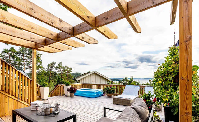 En soffgrupp står utomhus på ett trädäck under en pergola med bladskarvar. 
