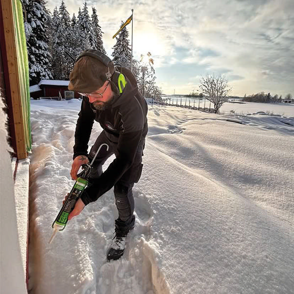 Snickare står i decimeter hög snö vid ett hus och håller i en patronspruta med ESSTACK Nordic Pro. 
